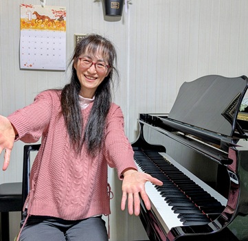 ピアノの前で笑顔の菊美先生